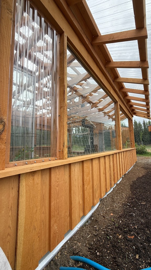 Side view of a rough cut lumber greenhouse with corrugated roof panels
